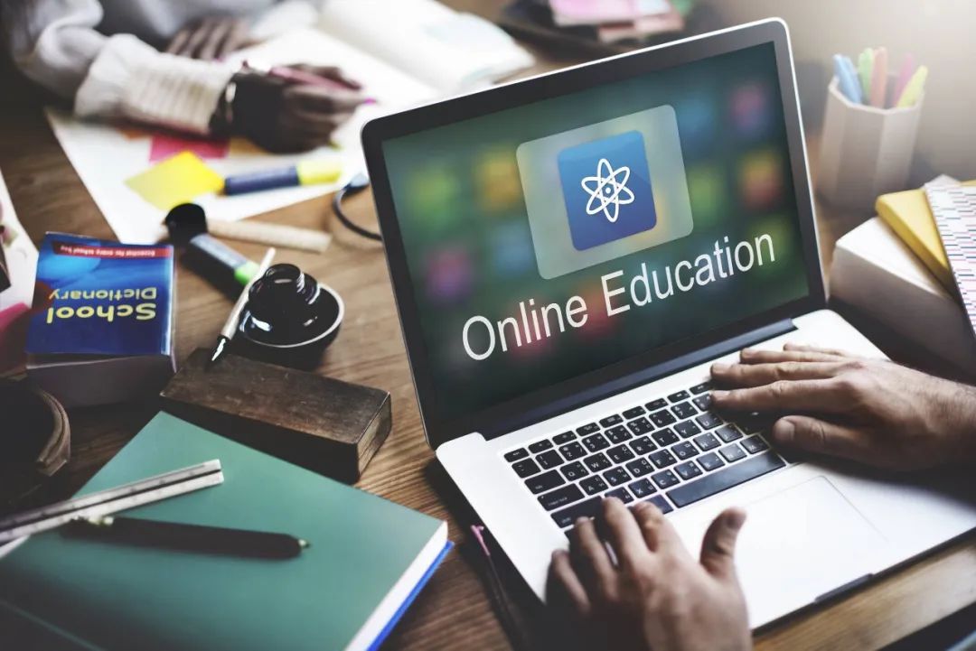 图片展示了一台笔记本电脑屏幕上显示“Online Education”字样，周围散布着书籍、笔记和耳机，体现了在线学习的环境。